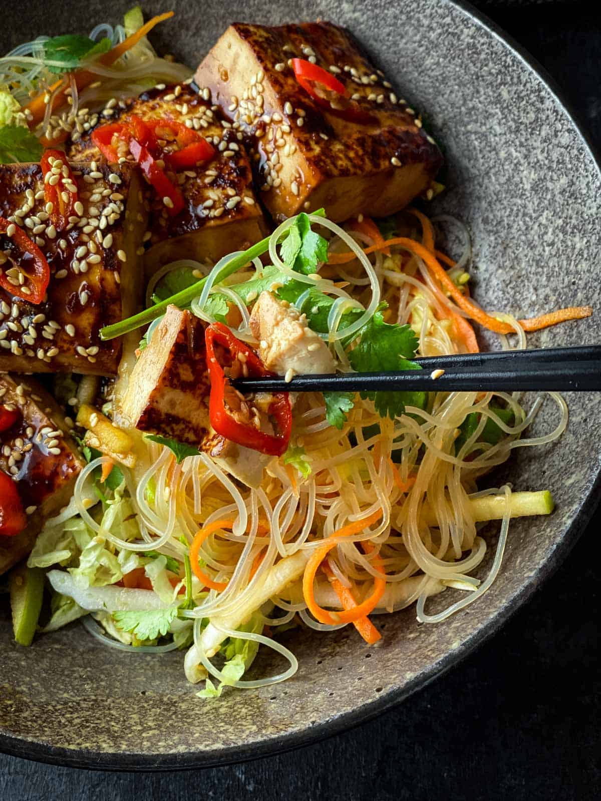 Using chopsticks to grab a serve of Glass Noodle Salad with Sticky Tofu from a bowl
