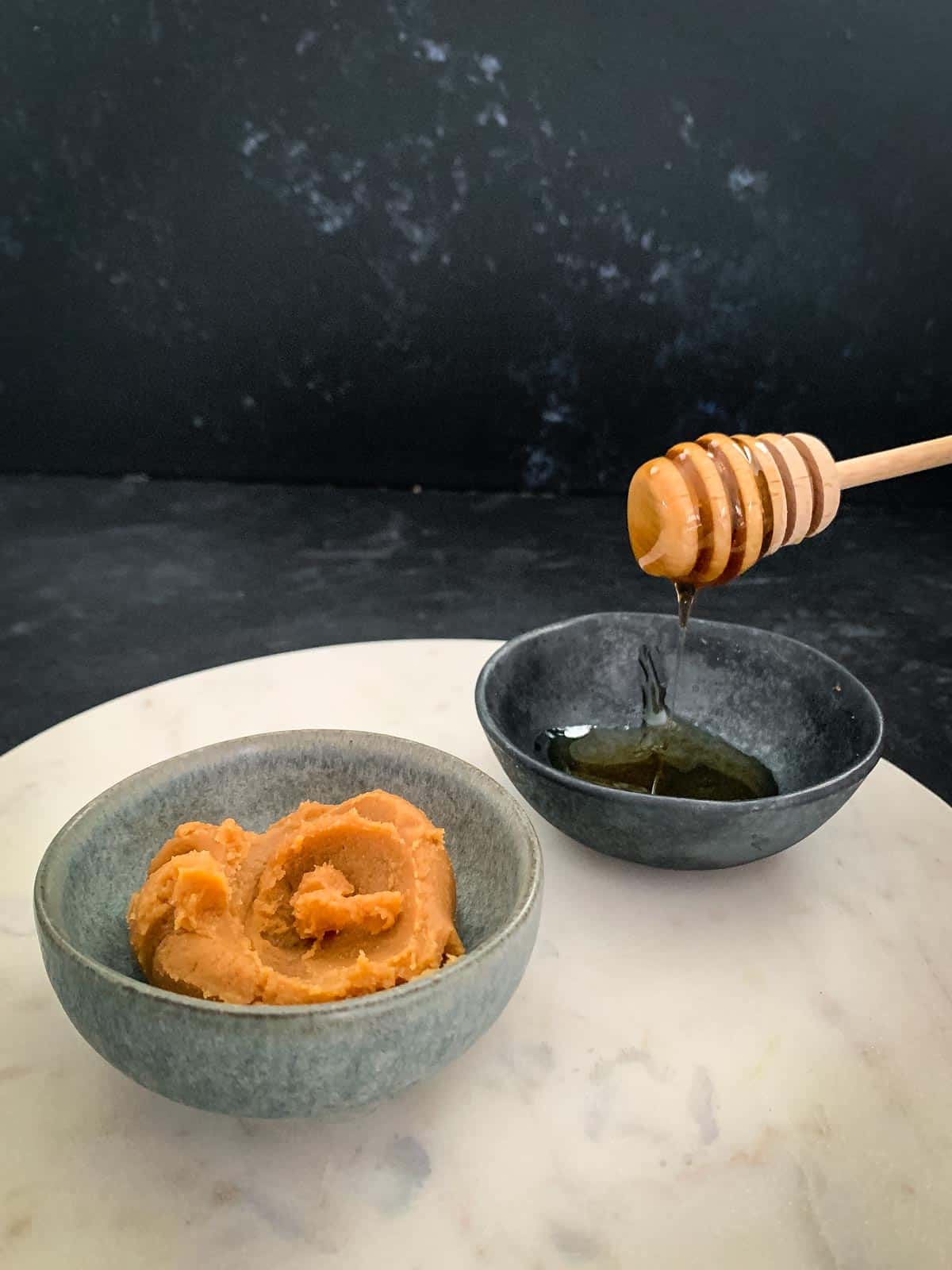 Miso paste and honey dripping off from a honey dipper, place on a white marble slab