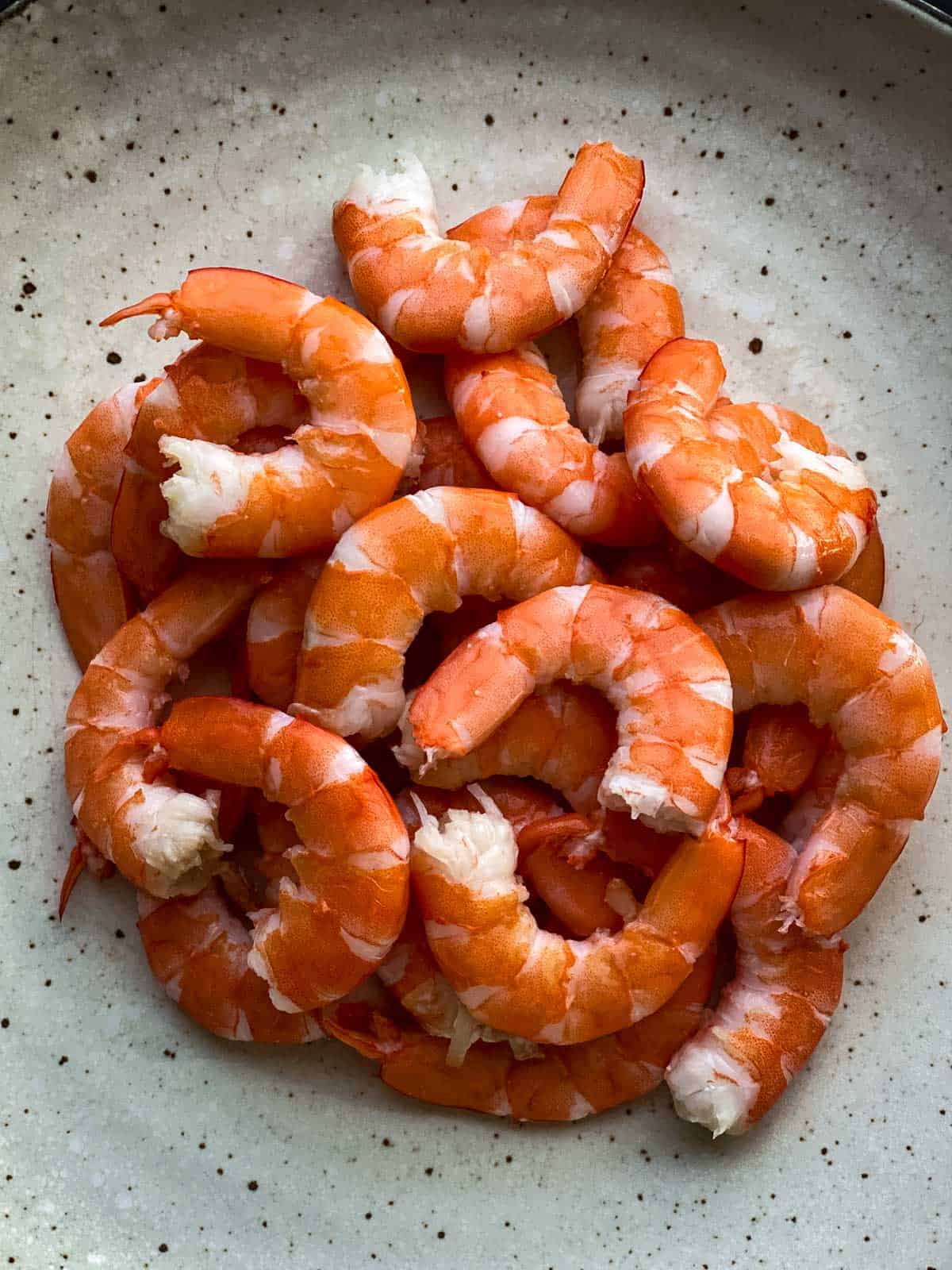 A heap of peeled prawns or shrimp on a grey plate