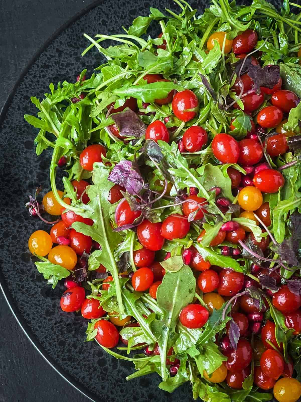 Tomberry Salad with Pomegranate on a black plate