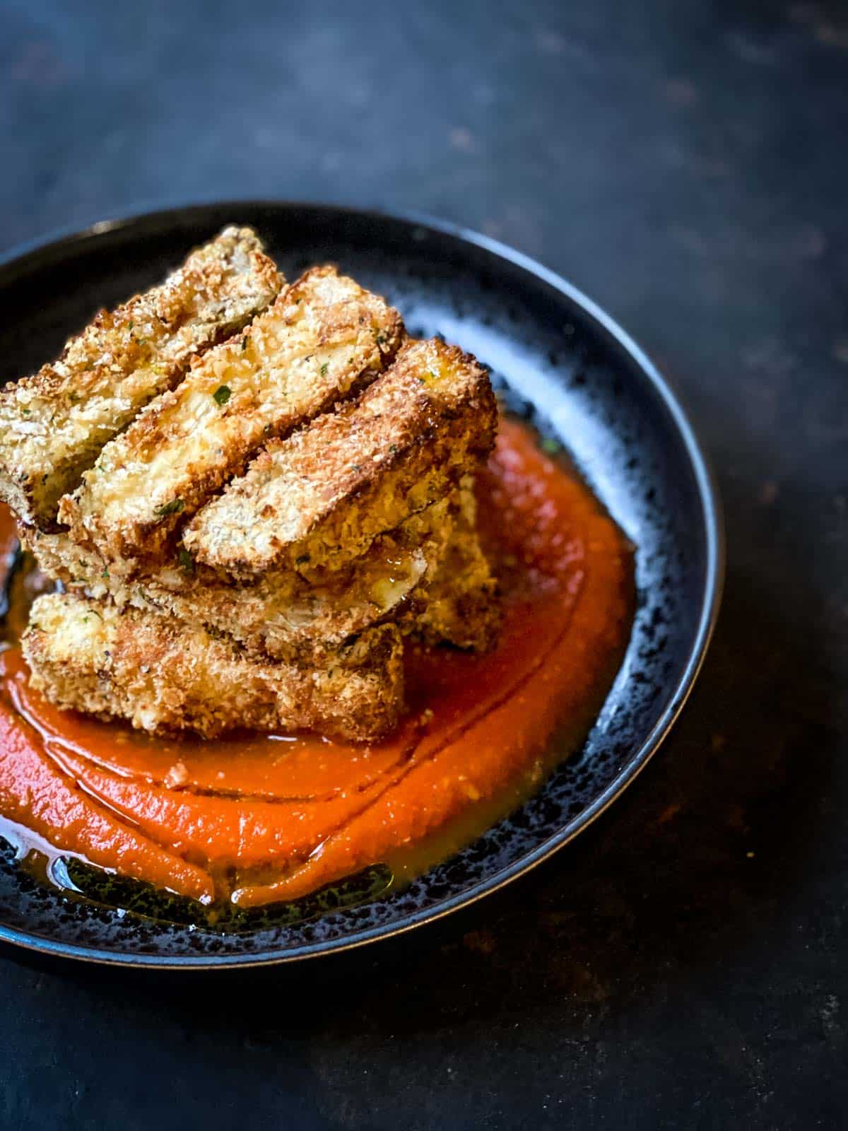 Air Fryer Eggplant with Roasted Red Pepper Sauce served in a black shallow bowl
