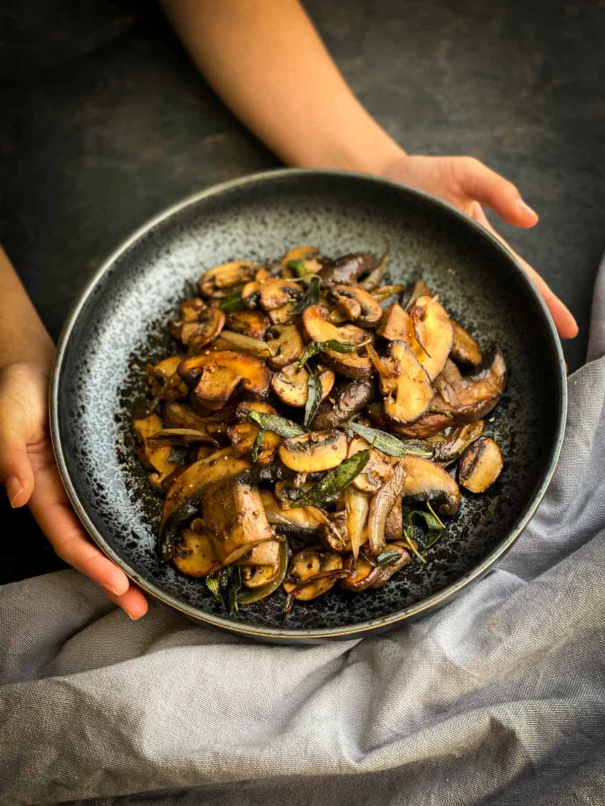 2 hands hold a plate of Easy Sauteed Mushrooms with Soy Sage Butter