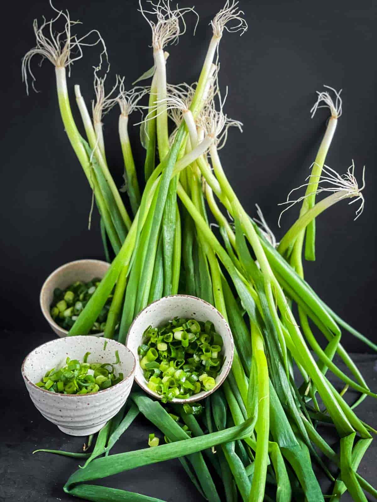 3 bowls of chopped scallions against a backdrop of whole scallions
