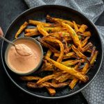 Air Fryer Parsnip Fries in a black speckled bowl with red pepper mayo sauce and dotted napery