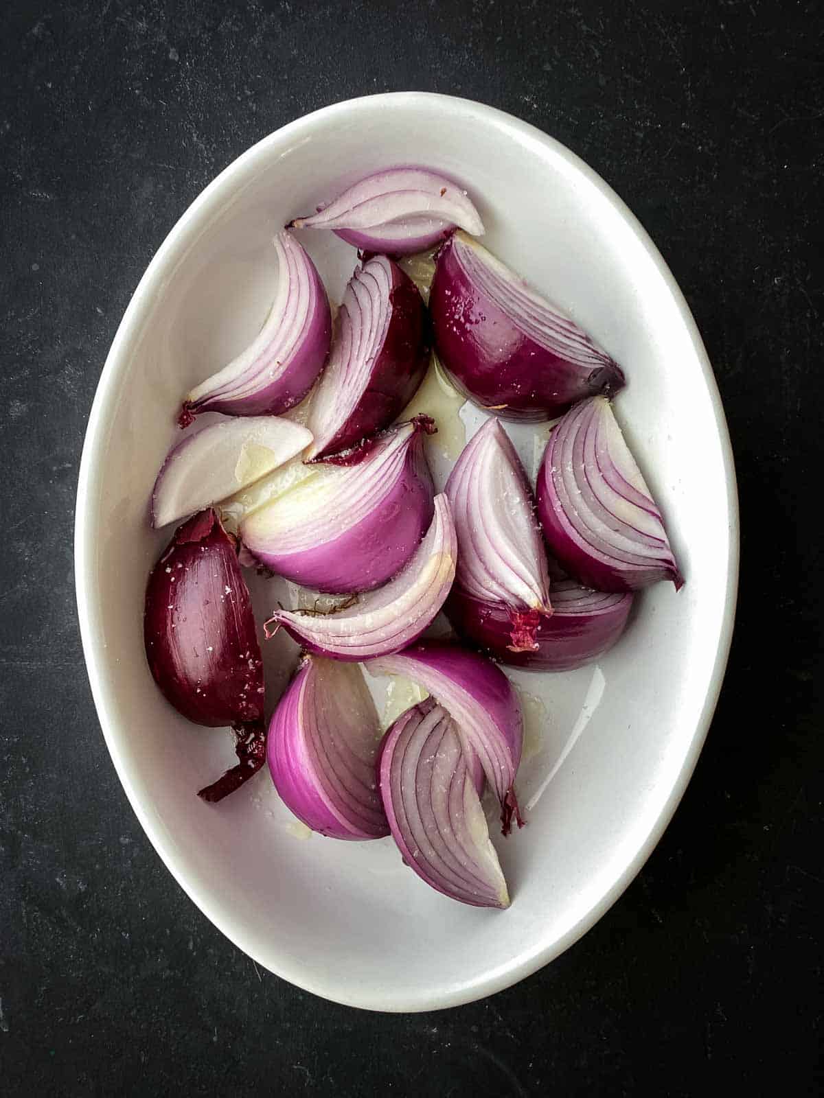 Wedges of roasted red onions in an oval ceramic baking dish
