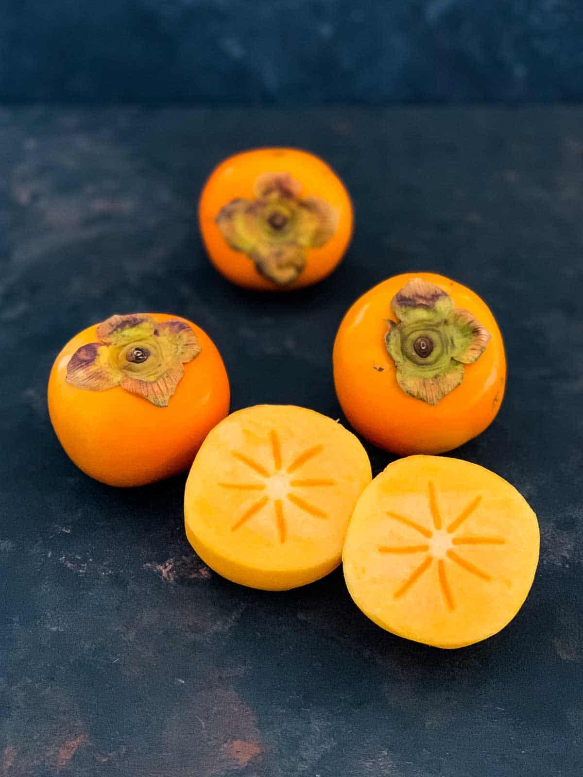 Whole fuyu persimmons and peeled and halved persimmons to show the star pattern in the middle