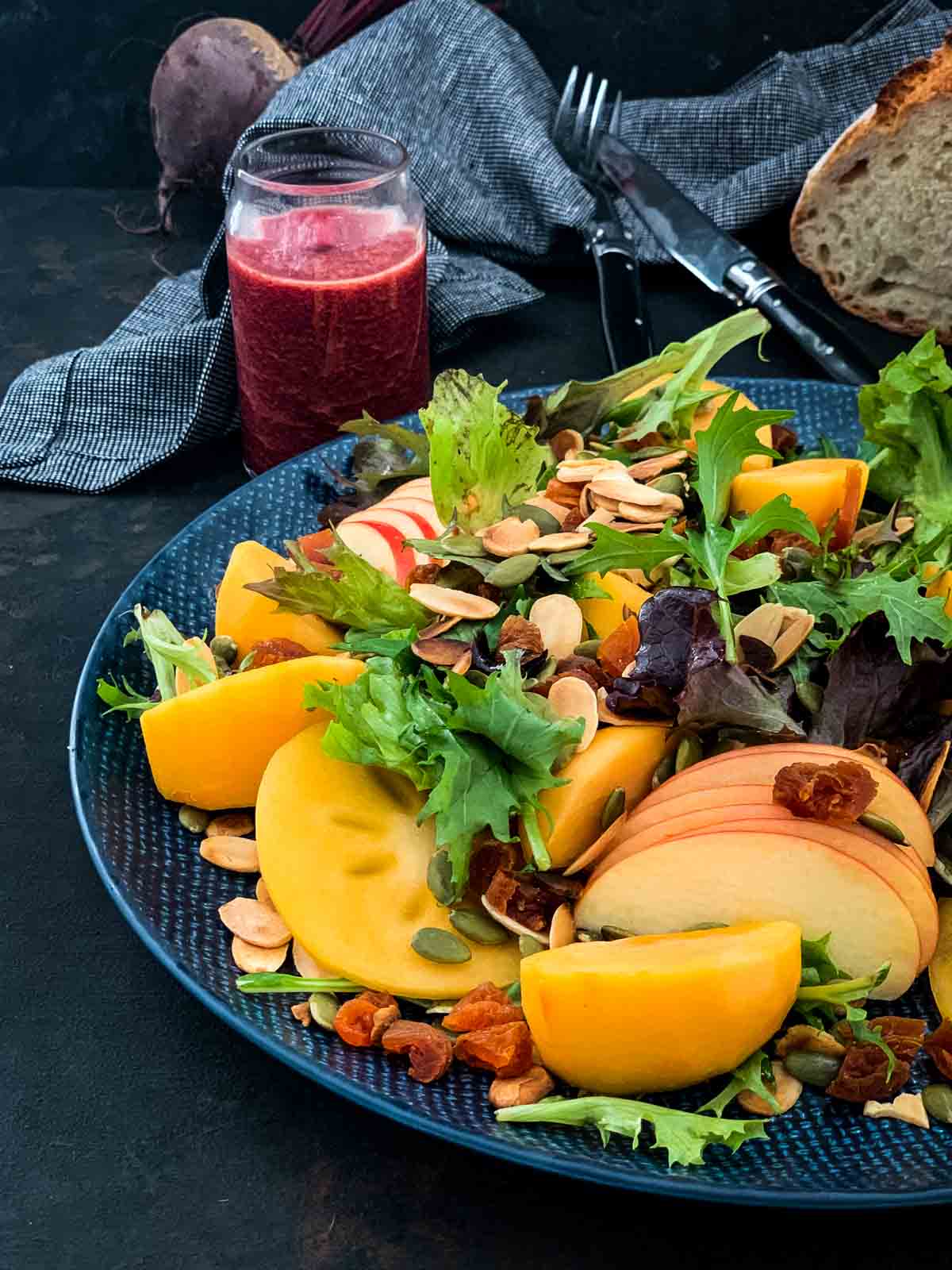 Salad with Persimmons and Beetroot Dressing on a blue plate with whole beetroot and some fresh bread