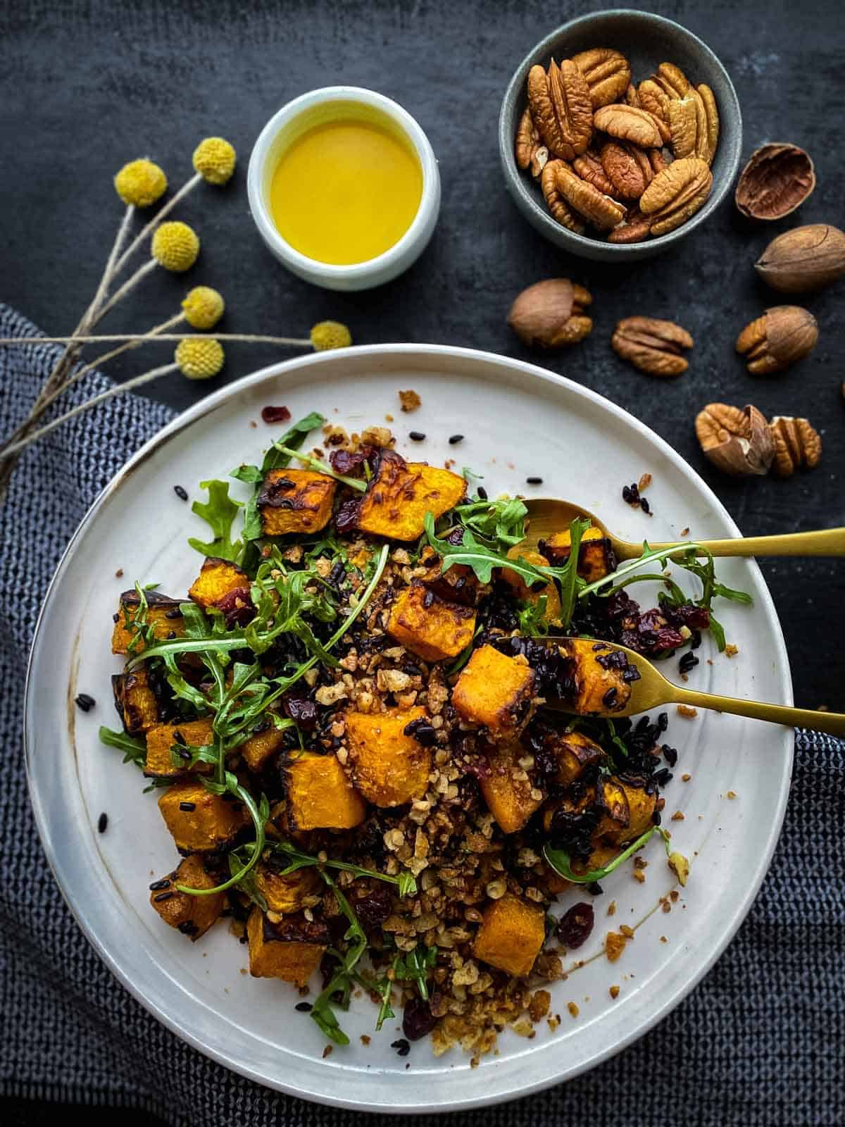 Vegan Salad with Butternut Squash and Cranberries on a marble plates with gold cutlery and dried yellow flowers