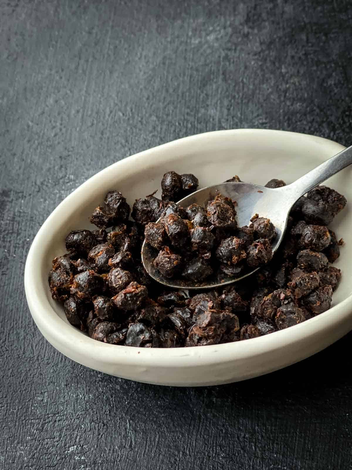Fermented black beans in a small bowl being scooped out by a teaspoon