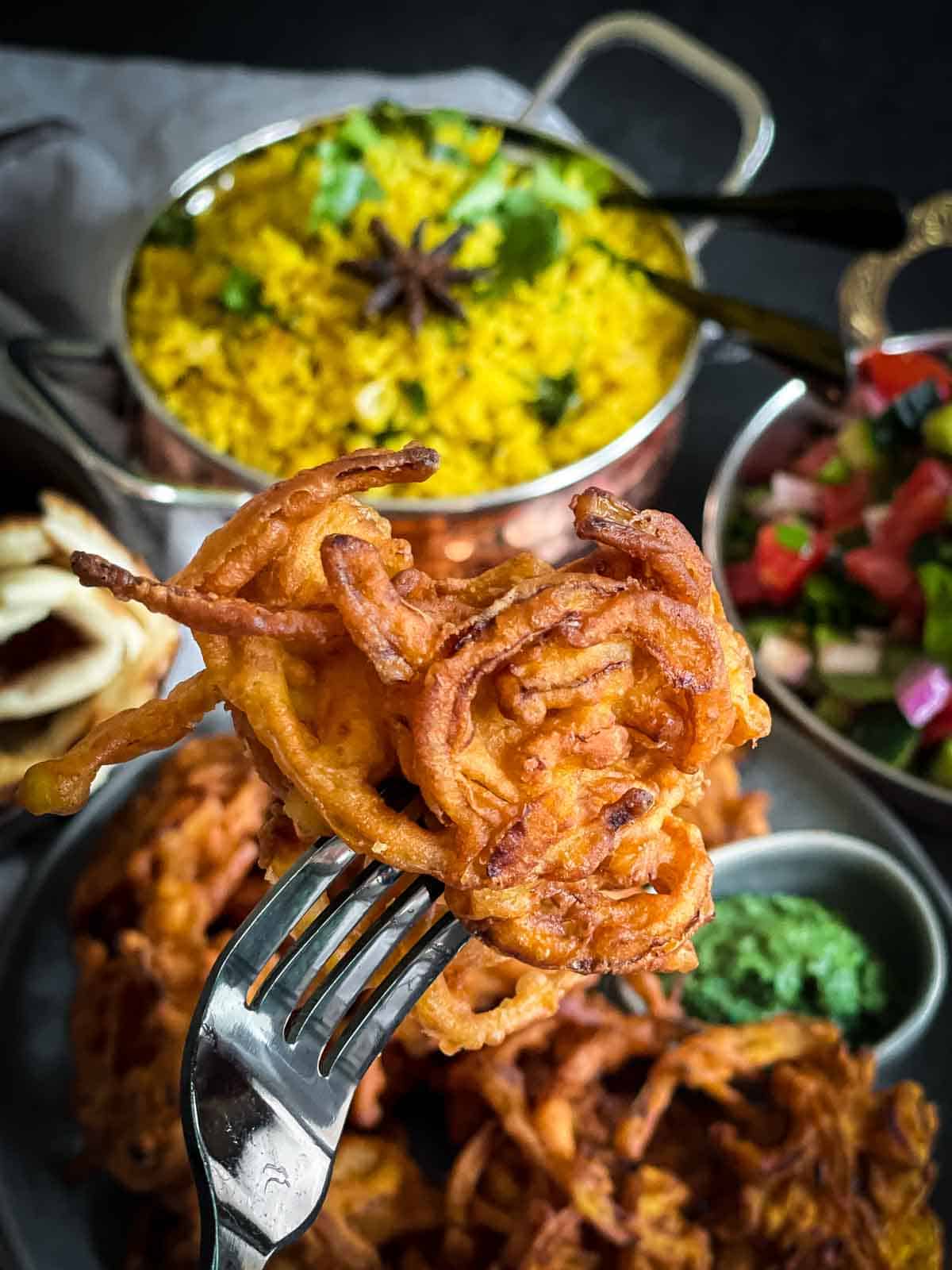 Close up of an onion bhaji on a fork served with turmeric rice, coriander chutney and kachumber