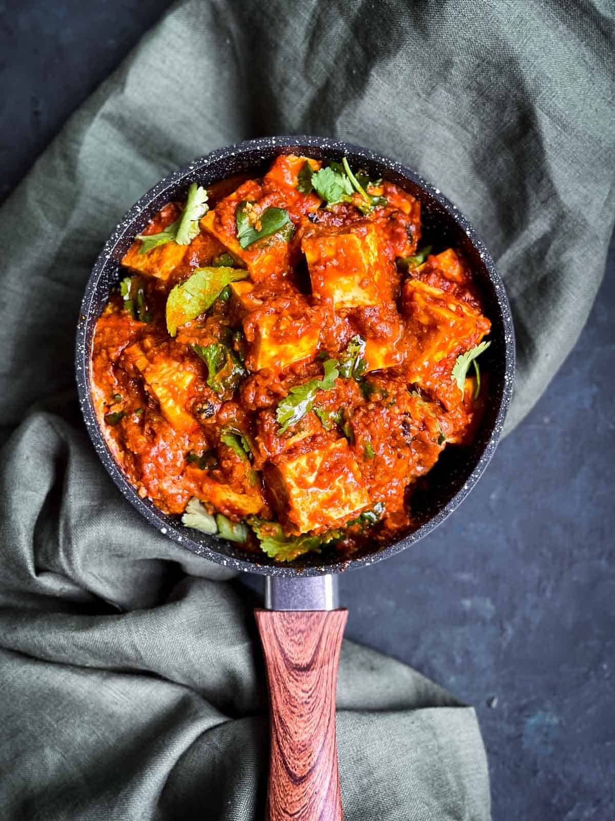 Paneer Butter Masala in a pot with a handle over green linen