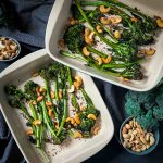 2 baking dishes of Roasted Tenderstem Broccoli and Garlic Cashews with blue napery