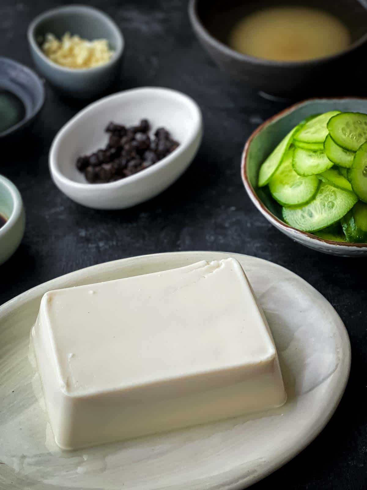 Silken tofu on an oval plate with black beans, cucumber, garlic and pickling juice