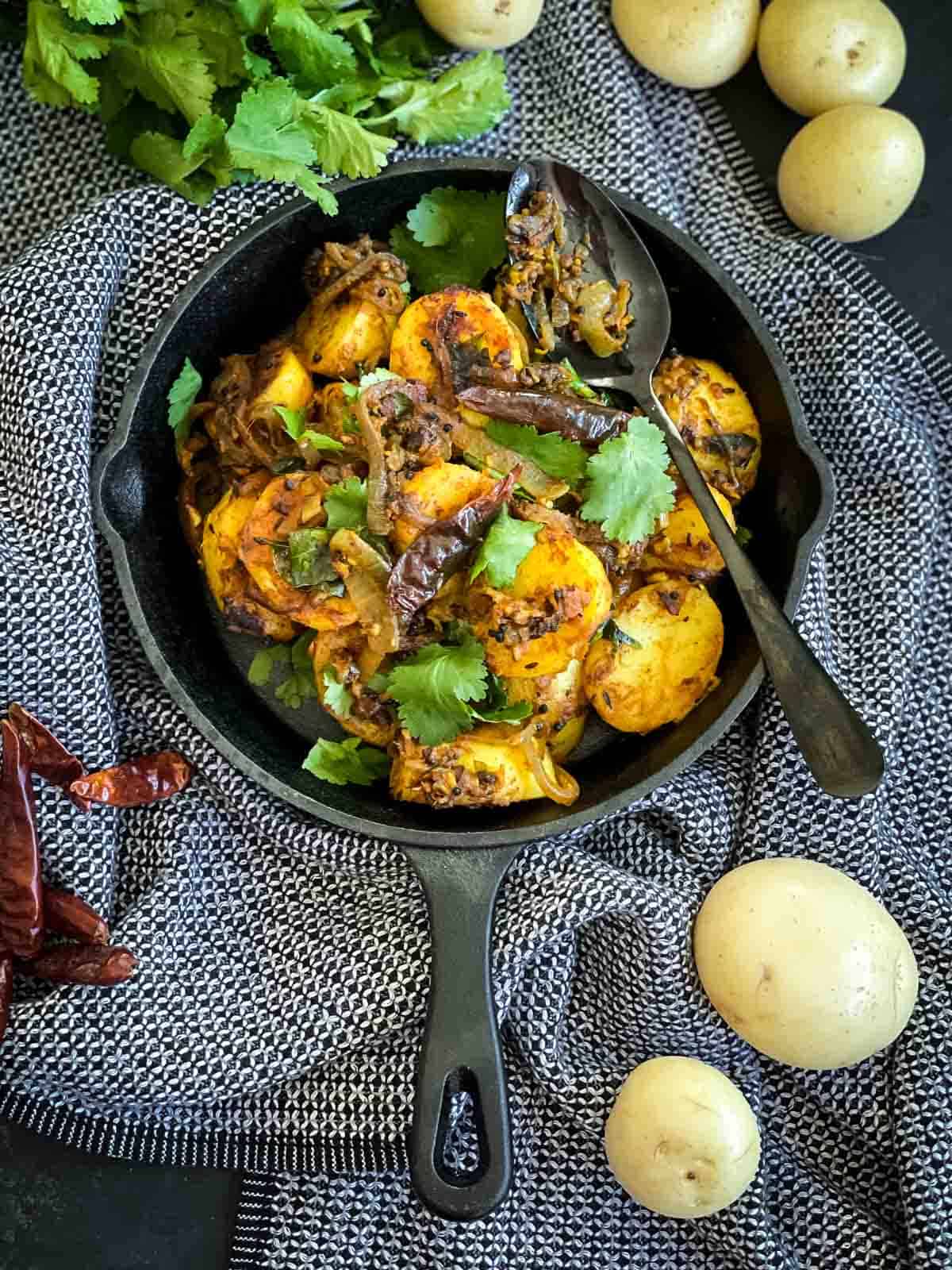 Bombay Aloo in a skillet with a black spoon on blue napery
