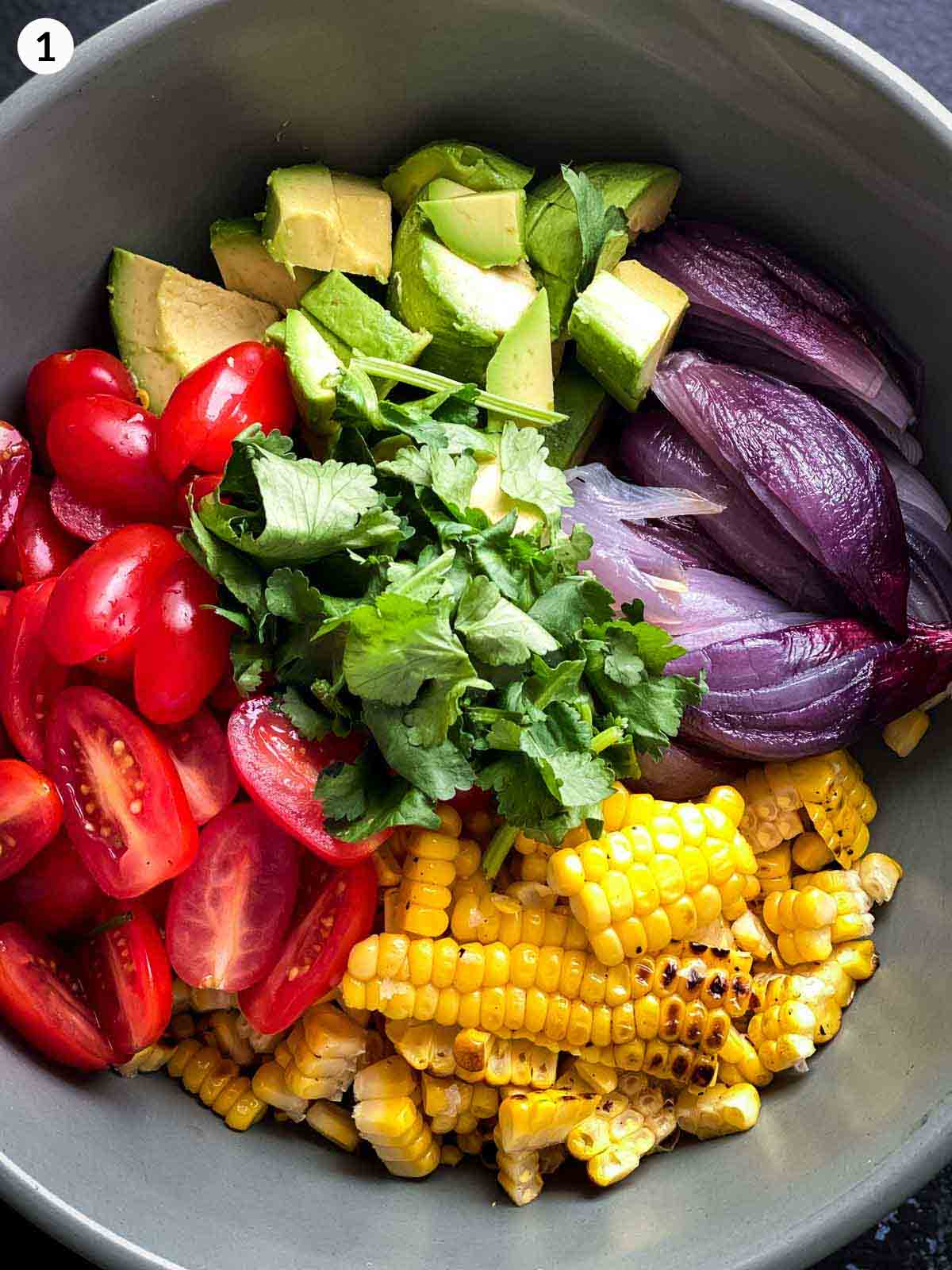 Cherry tomatoes, sliced charred corn, roasted onion wedges, avocado and coriander in a grey bowl