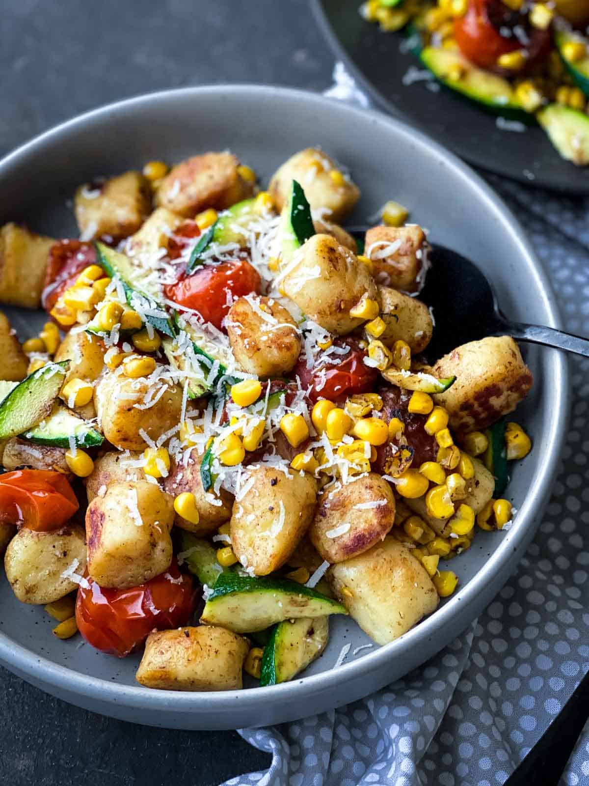 Pan Fried Gnocchi with Tomato, Corn and Zucchini in a grey bowl with dotted linen