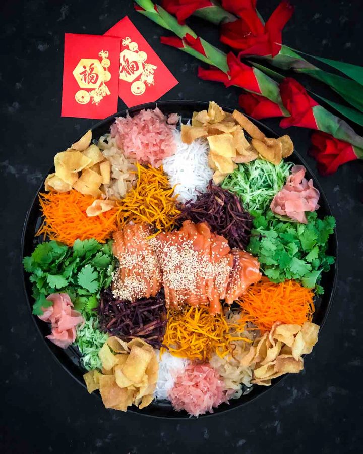 Yee sang platter decorated with Chinese red packets and red gladiolus flowers