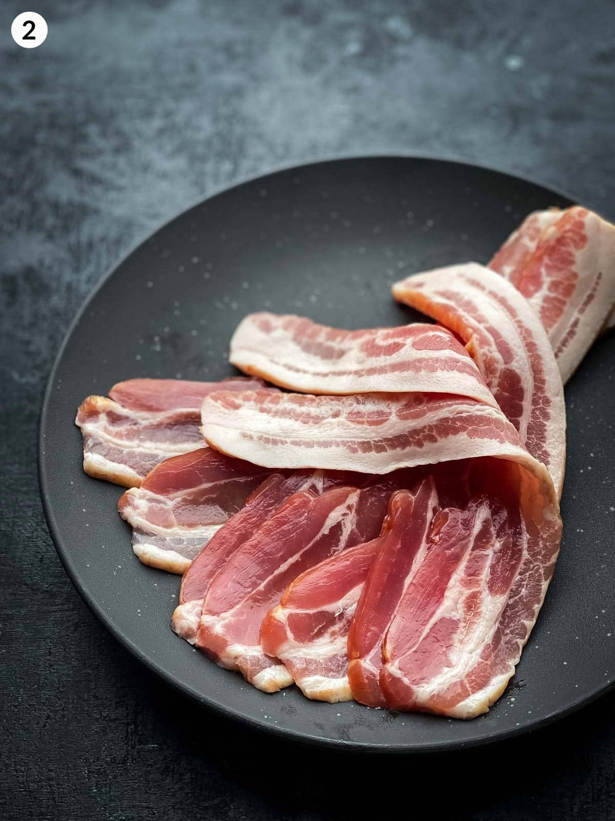Streaky bacon on a black plate