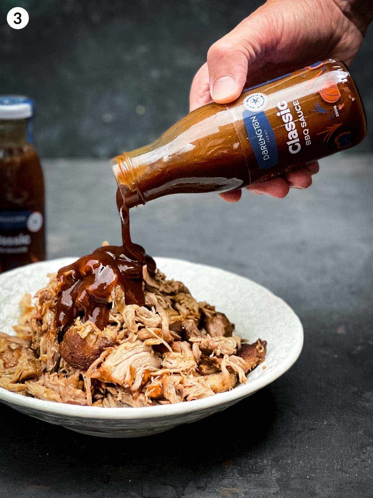 Hand pouring BBQ sauce over pulled pork