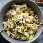 Potato salad in a large grey bowl with 2 spoons inside