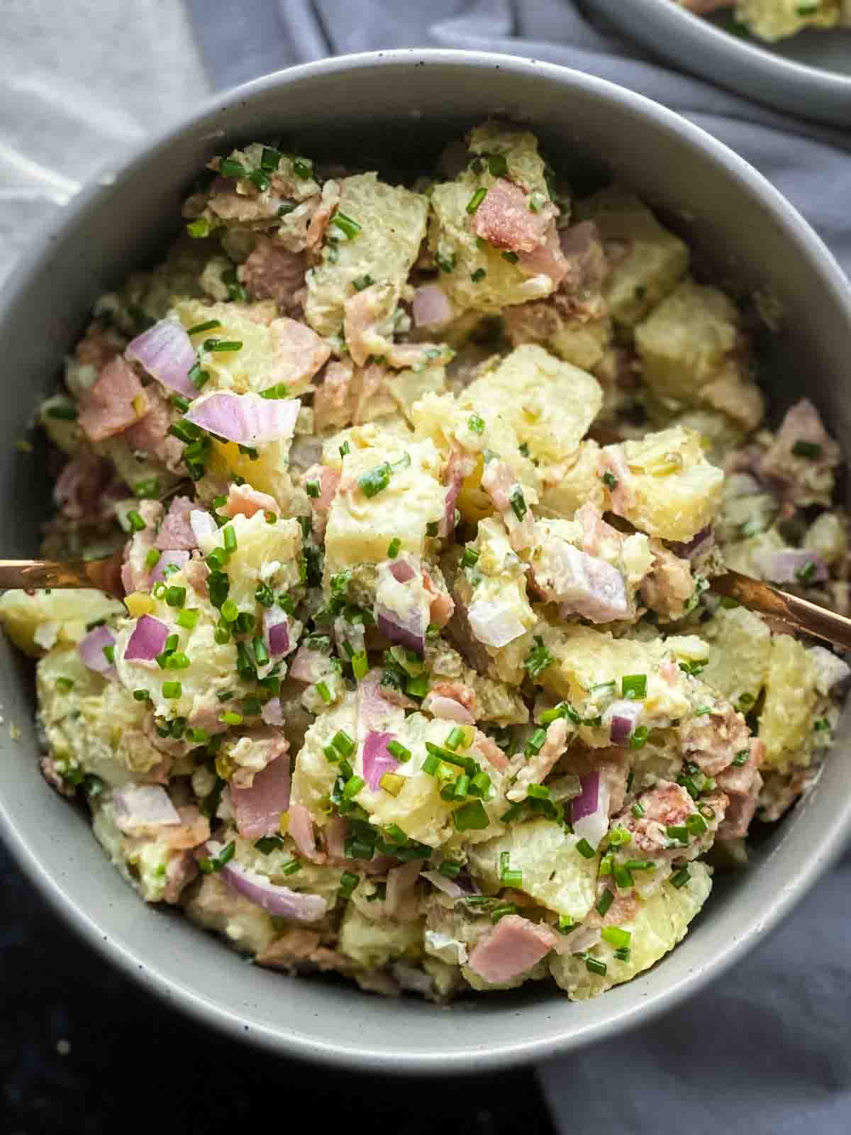 Potato salad in a large grey bowl with 2 spoons inside