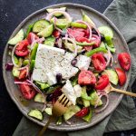 Greek salad with fork and spoon on a plate.