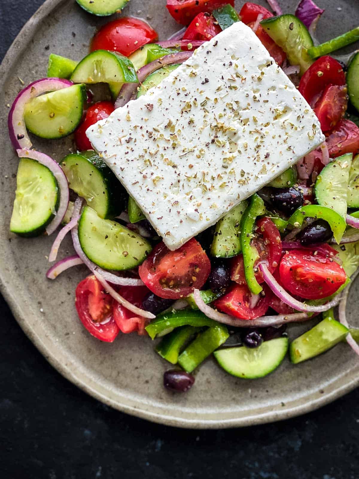 Easy Greek Salad Recipe with a whole block of feta cheese on a brown plate