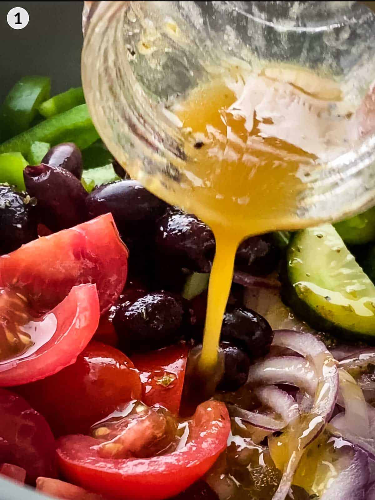 Pouring oregano vinaigrette from a jar onto Greek salad