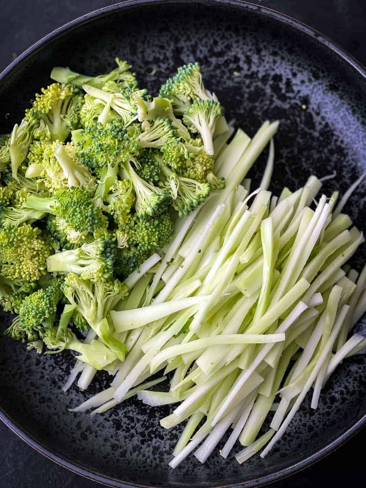 Small cuts of broccoli florets next to match stick broccoli stems on a black plate.