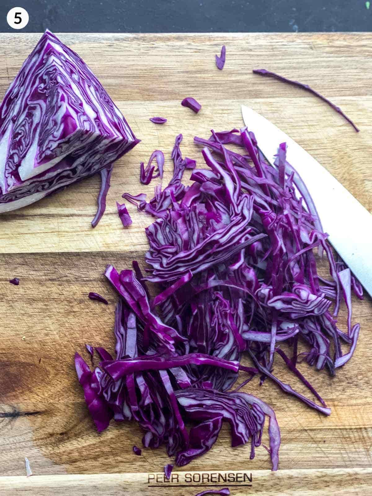 2 hands shredding red cabbage with a knife on a chopping board