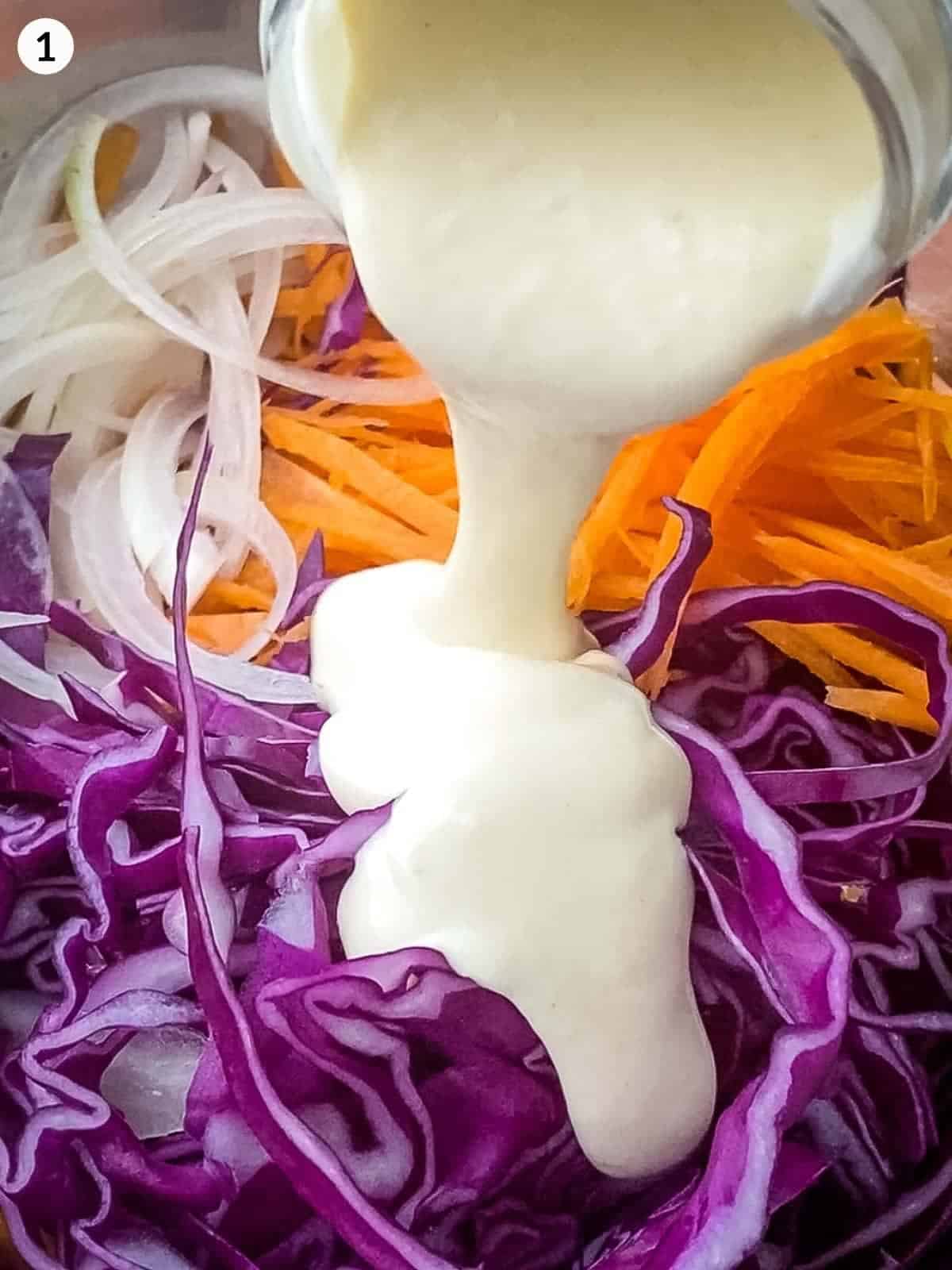 Pouring coleslaw dressing over cabbage, onions and carrots