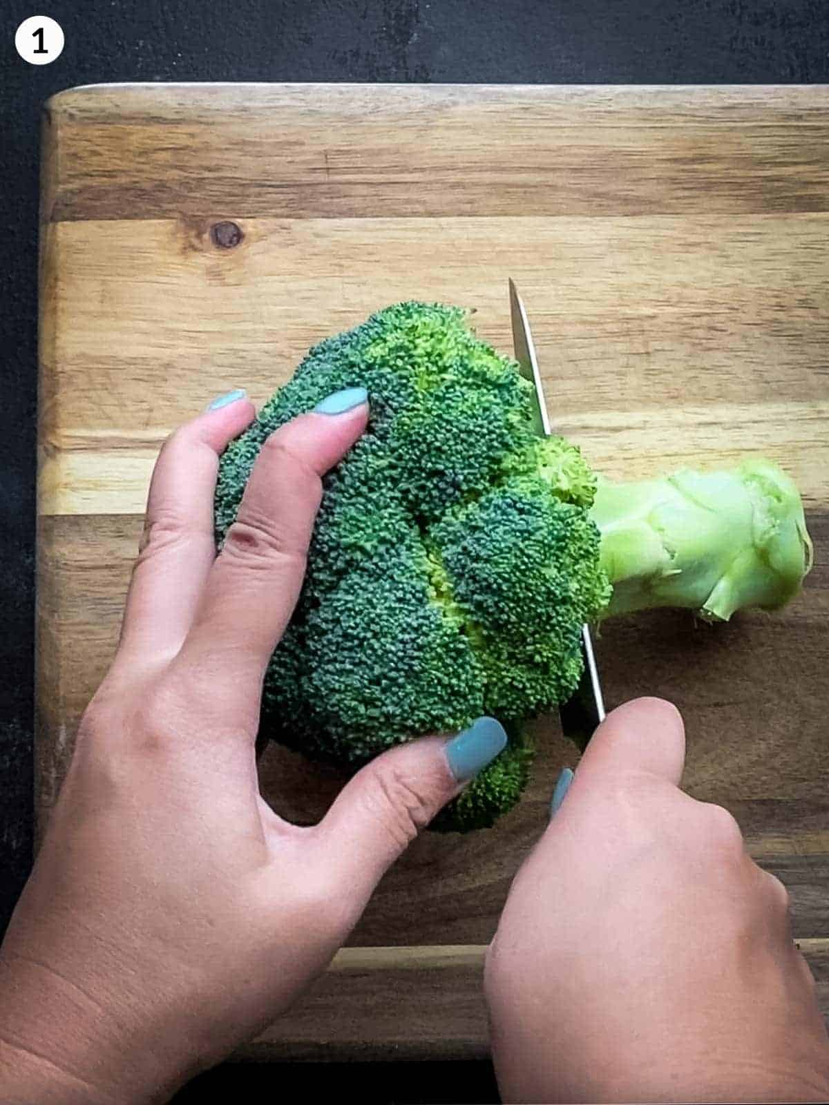 Cutting off the stem of a broccoli with a knife on a wooden chopping board