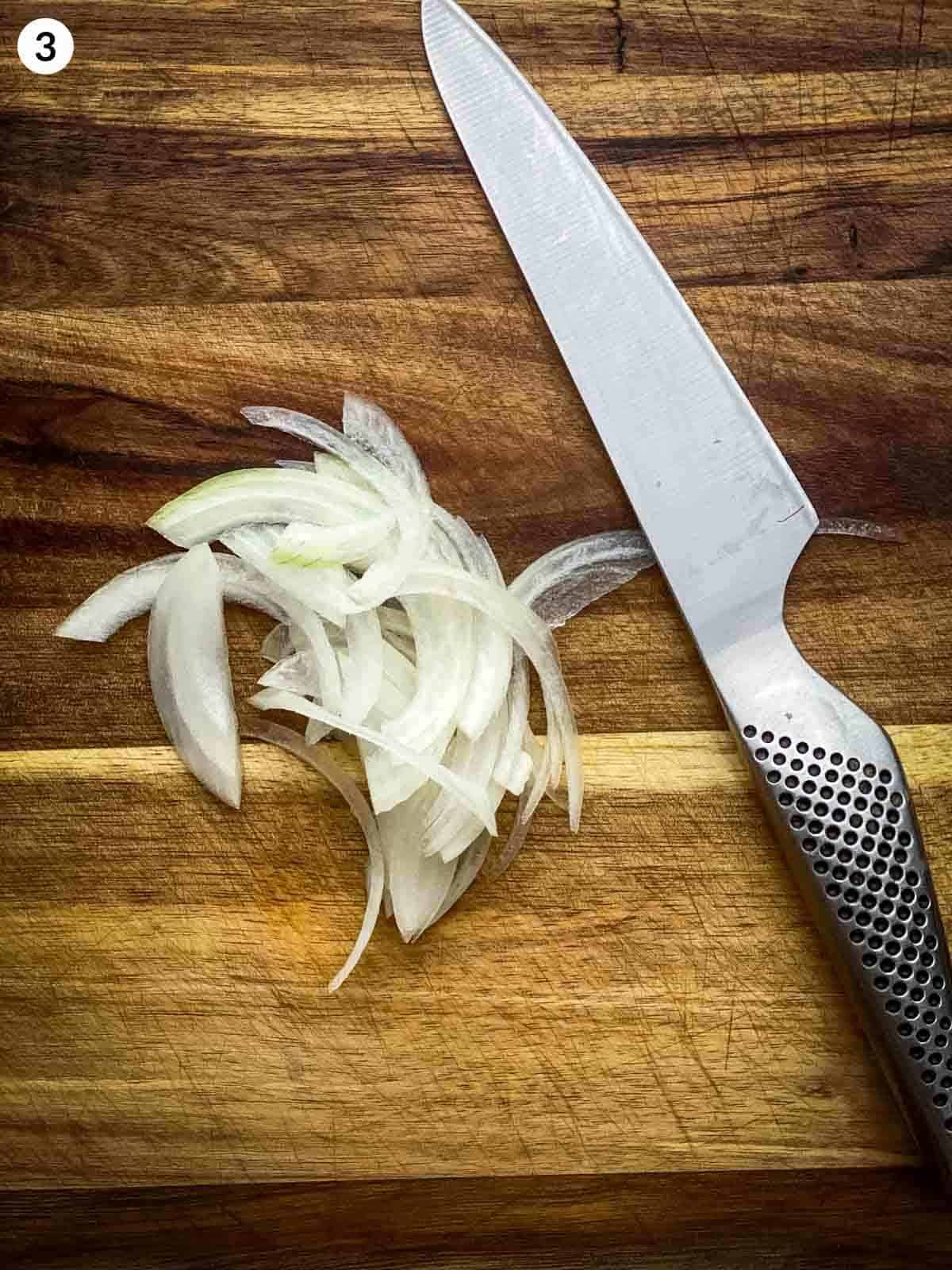 slicing onion with a knife on a wooden chopping board