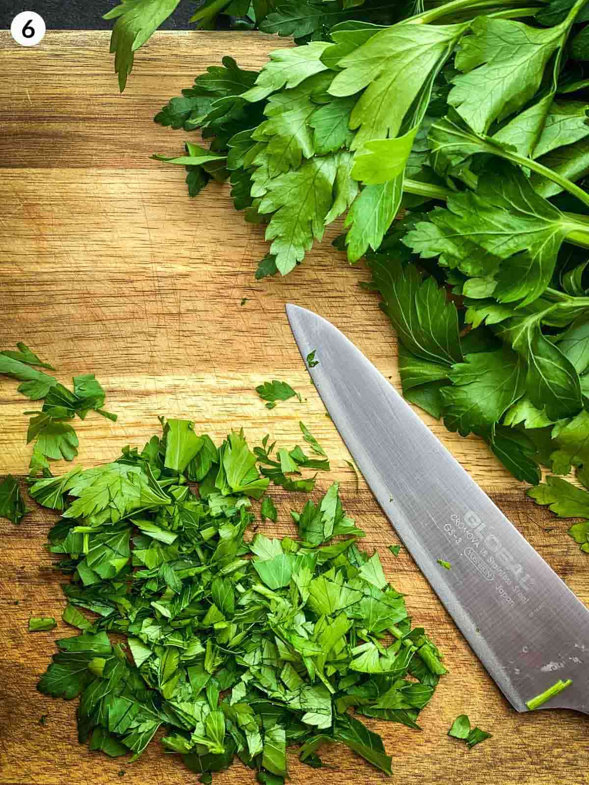 Cutting parsley with a knife on a wooden chopping board