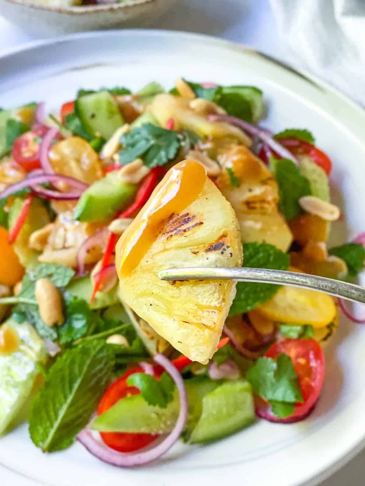 a fork holding a grilled pineapple piece with peanut dressing on the top