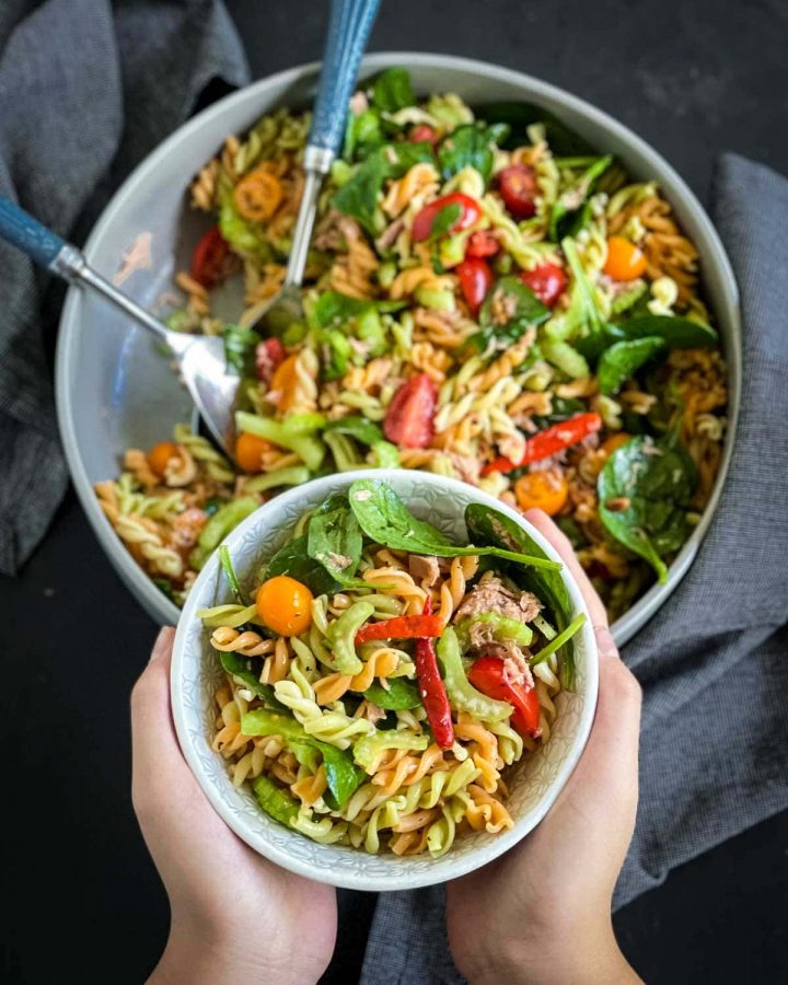 2 hands hold a small bowl of tuna pasta salad, hovering over a larger bowl below.