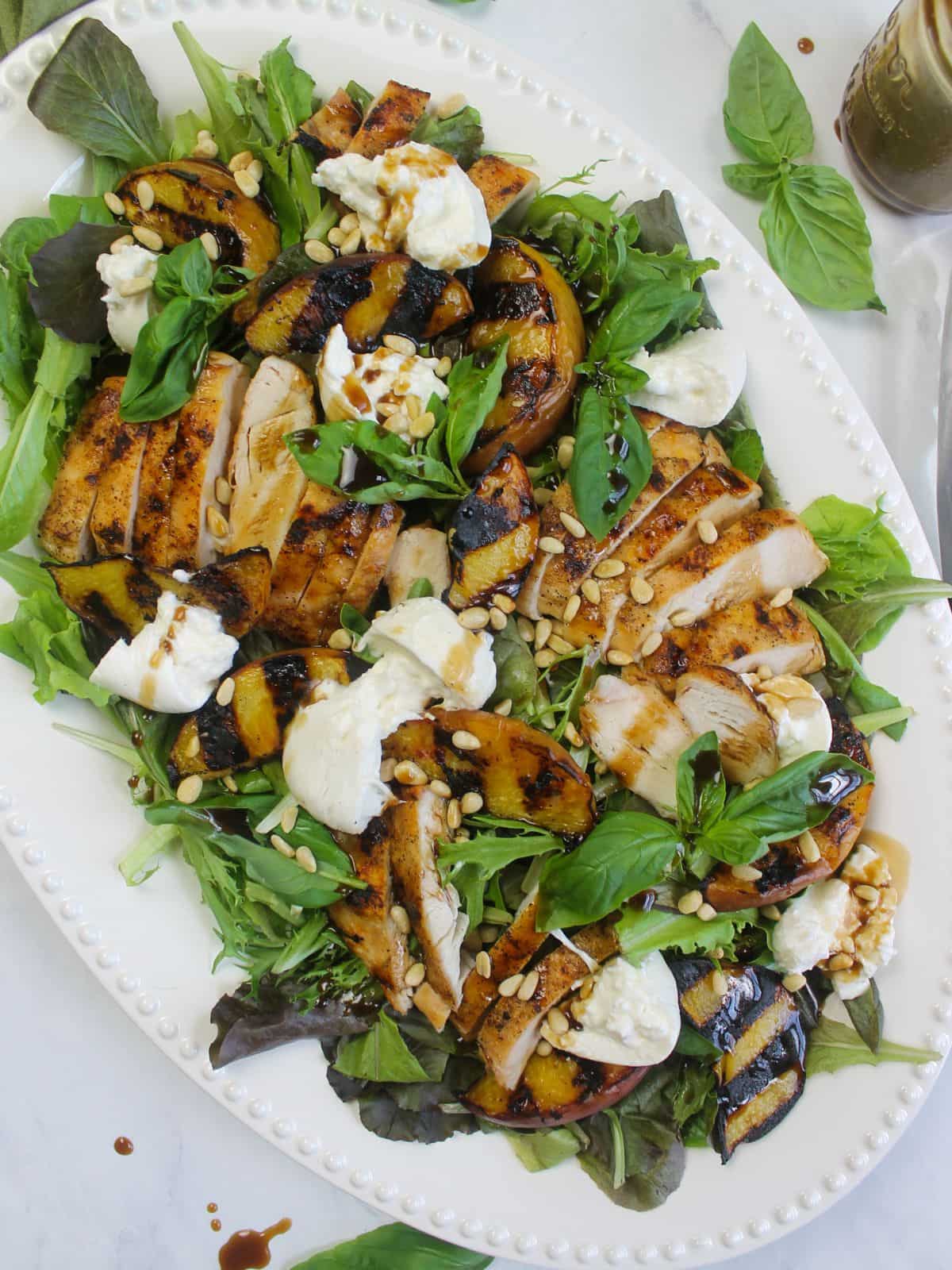 grilled peah and burrata chicken salad served on an oval white platter