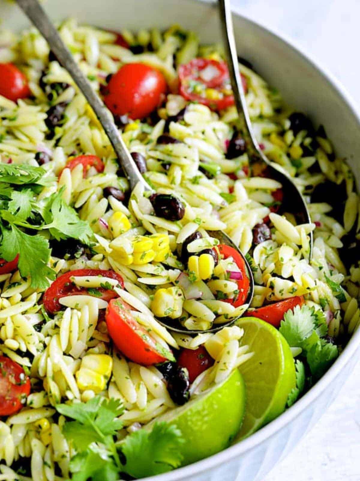 Southwestern Orzo Pasta Salad with Cilantro Lime Dressing in a white bowl with salad serving cutlery