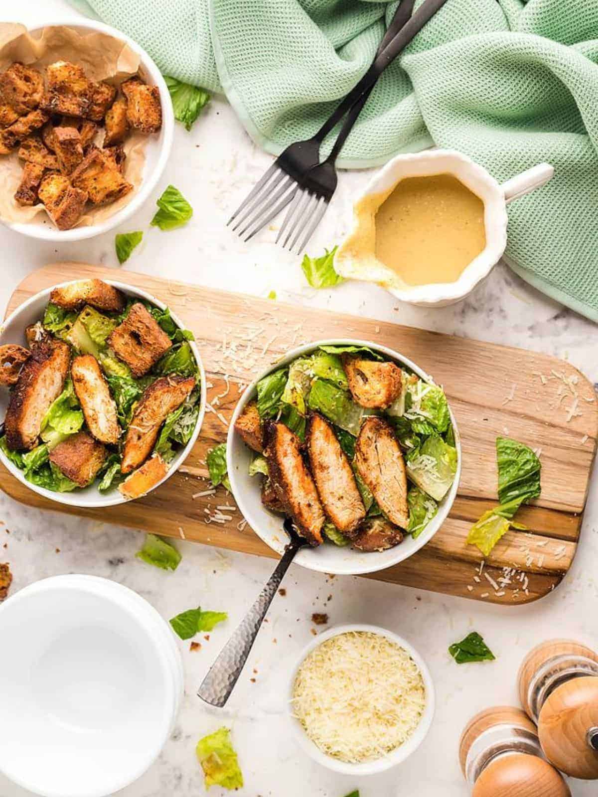 2 bowls of Air fryer blackened chicken salad served on a wooden boardwith serve of dressing and cheese on the side