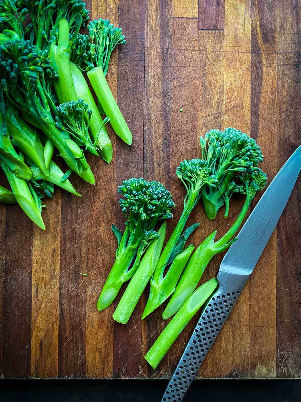 Slicing broccolini with a knife on a wooden chopping board