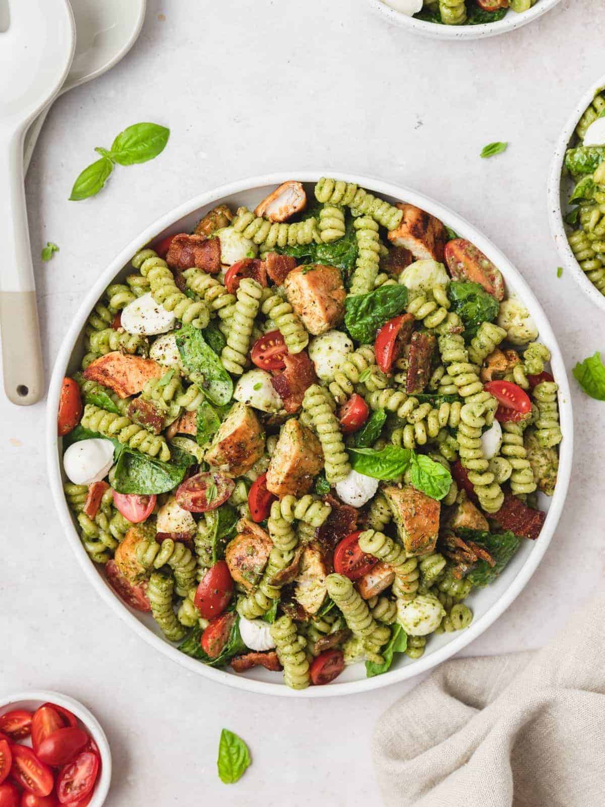 chicken pesto pasta salad in a white bowl and white salad serving spoons