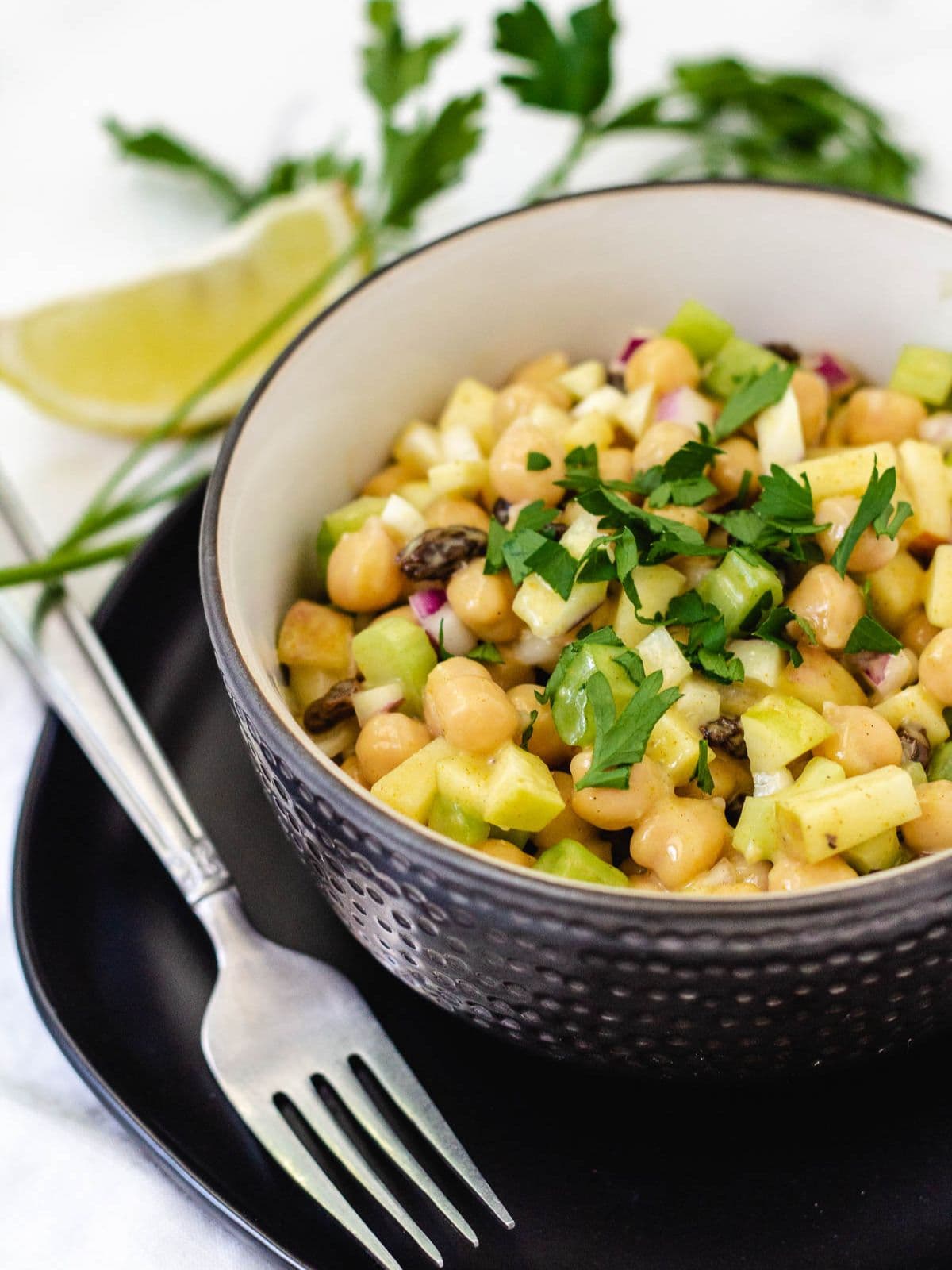 Chickpea curry salad in a black bowl served on a black plate and a silver fork to the side