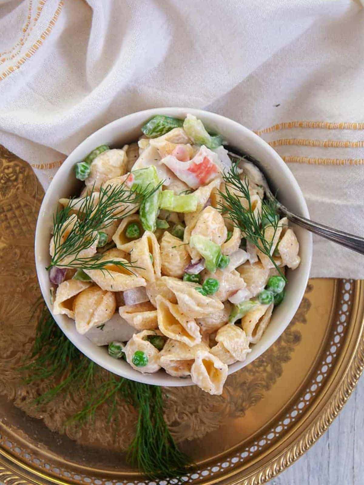 crab pasta salad in a white bowl served on top of a vintage bronze tray and white napkin