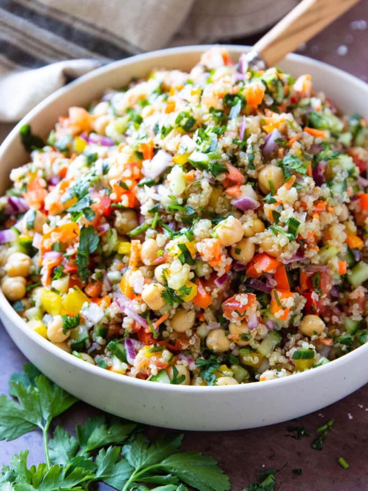 Quinoa chickpea salad in a white salad bowl with a wooden spoon