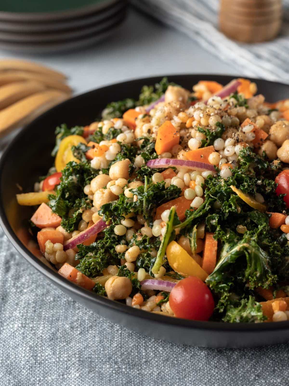 Spicy kale couscous chickpea salad in a black bowl on grey linen