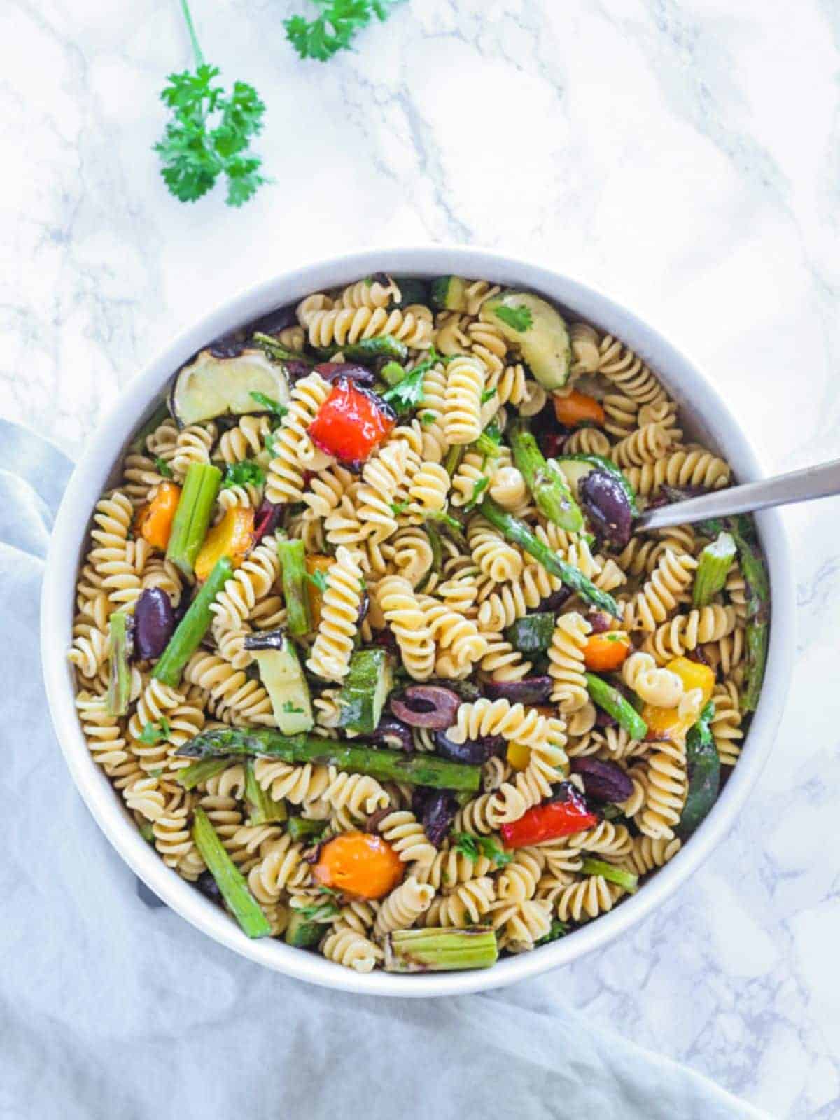 grilled vegetable pasta salad in a white bowl with a spoon inside the pasta