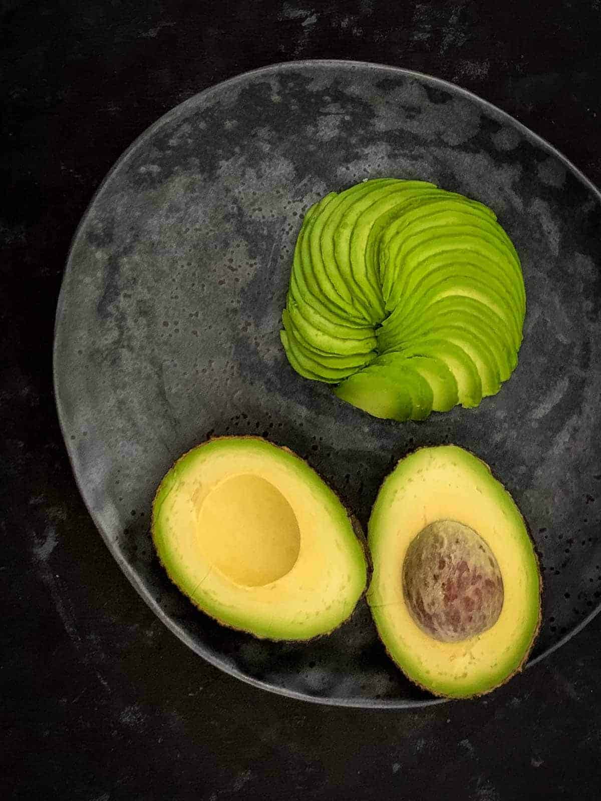 2 avocado halves and an avocado fan on a grey plare