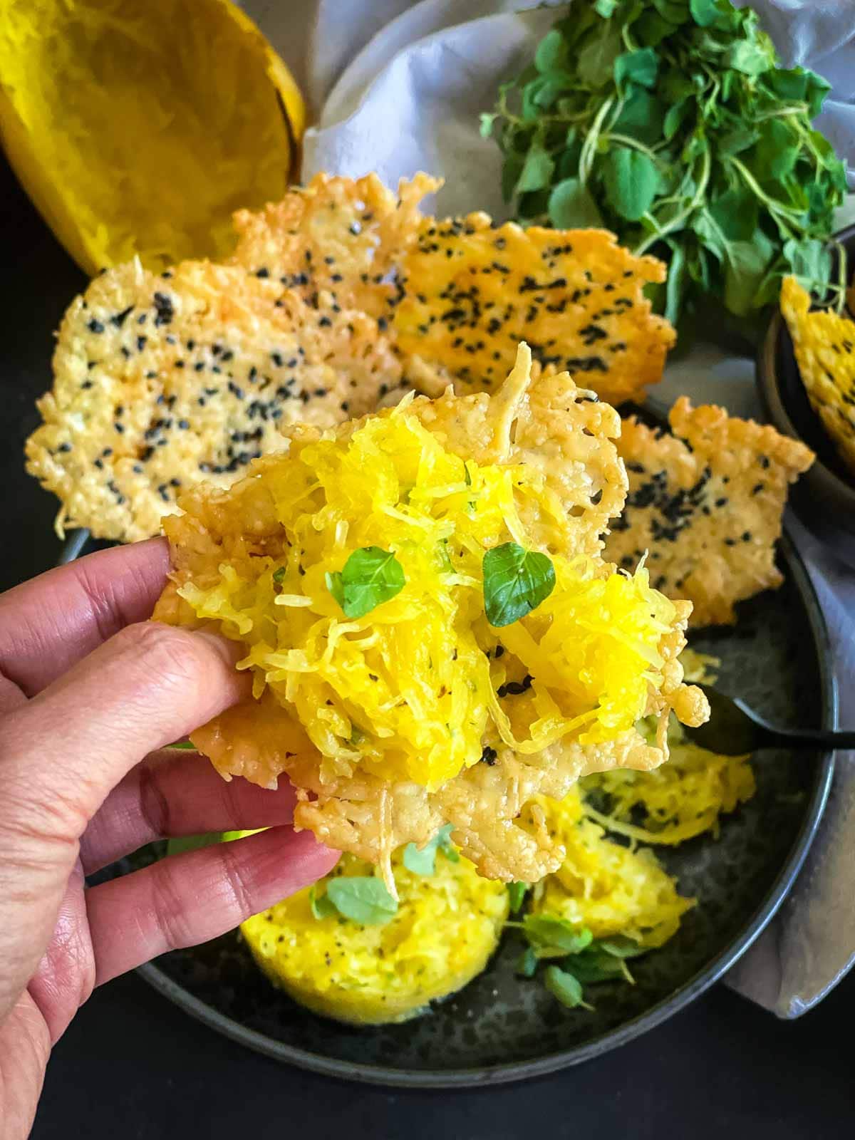 Hand lifting a serve of the buttered spaghetti squash onto a parmesan crisp