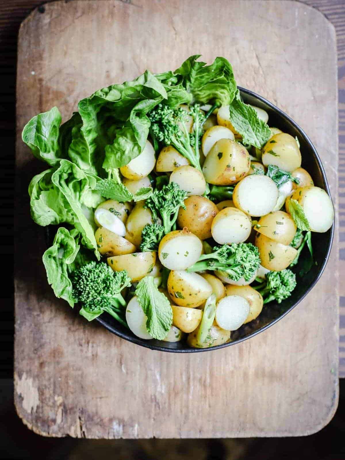 English mint potato salad in a black bowl served on a wooden board