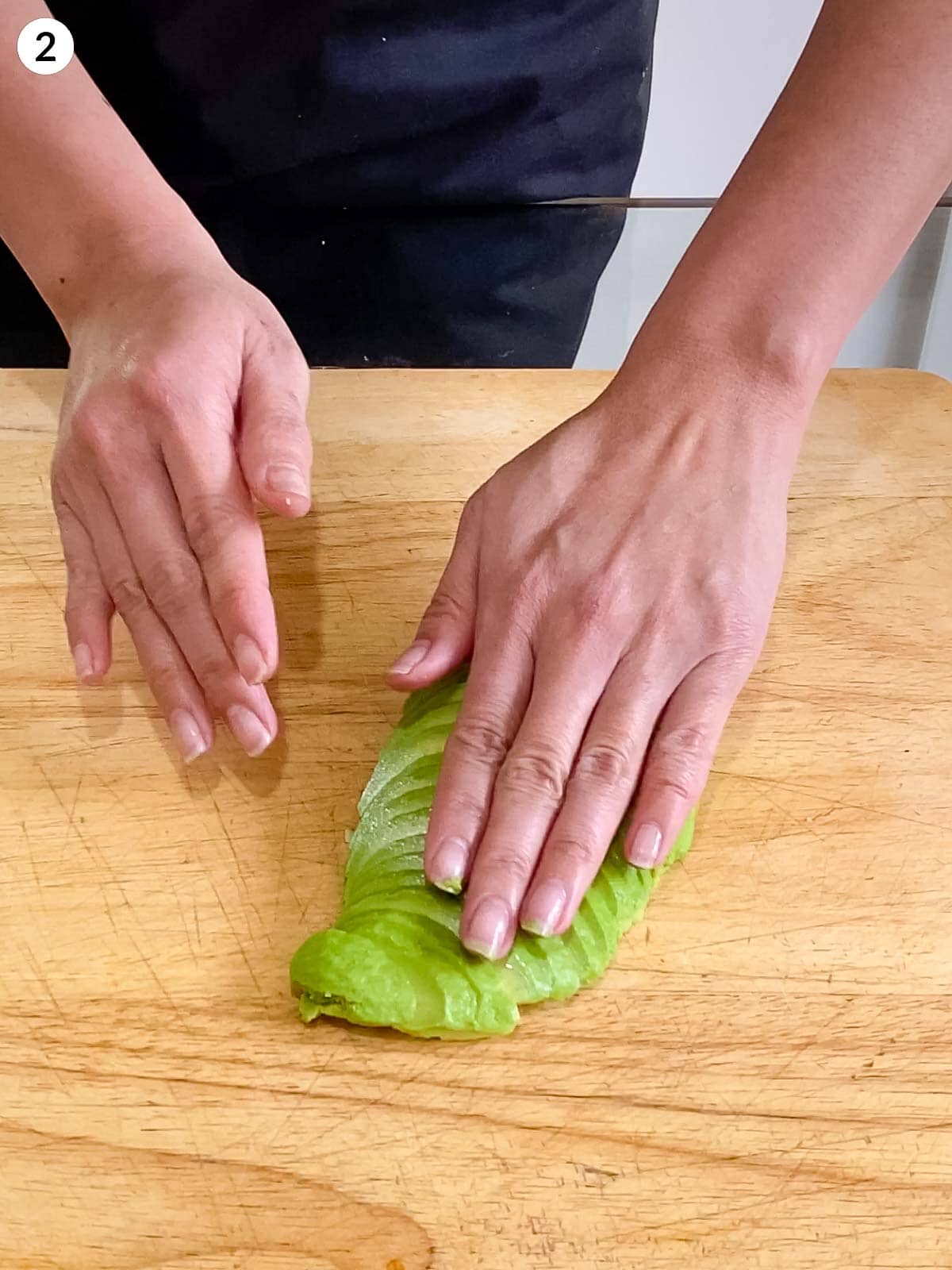 Person in an apron slicing avocado on a wooden chopping board